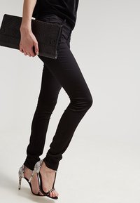 Černé skinny džíny v kombinaci s černým psaníčkem s krokodýlí texturou a stříbrně akcentovanými sandály na vysokém podpatku. Hladká látka s přiléhavým střihem.