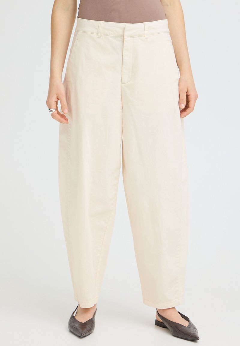 Pantalon crème taille haute coupe ample avec poches avant, porté avec des ballerines pointues foncées et un haut sans manches taupe.