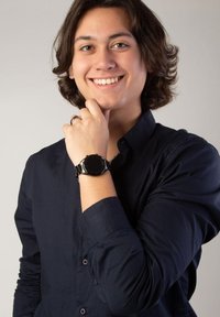 Zwarte smartwatch met een ronde wijzerplaat en een metalen band, gedragen om een pols, gecombineerd met een blauw overhemd met knoopmanchetten.