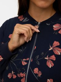 Navy bomber jacket with a floral pattern in pink and beige, featuring a front zipper and ribbed cuffs. Soft fabric with a smooth texture.