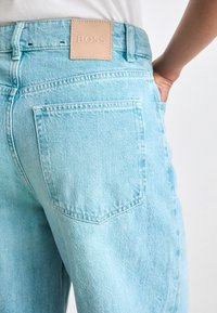 Lyseblå denimjeans med et lær BOSS-logo-patch, tradisjonell fem-lommers design, og en avslappet passform med synlige sømdetaljer.