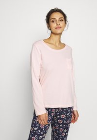 Lichtroze shirt met lange mouwen en een ronde halslijn, voorzien van een voorzak. Gepaard met donker bloemenpatroon broek. Zachte stofstructuur.