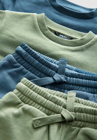 Drie kledingstukken: twee groene en één blauwe sweatshirt, en bijpassende blauwe en groene joggers. Zachte stof, geribde manchetten en details met trekkoorden.