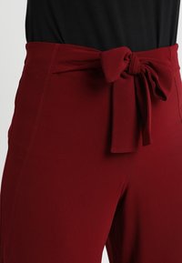 Rode broek met hoge taille en een geknoopte strikdetail aan de taille. Gemaakt van zachte stof, met een gladde textuur en een getailleerde pasvorm.