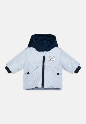 Giacca a vento leggera di colore blu chiaro con cappuccio blu navy, chiusura con zip, due tasche con bottone e un logo circolare sul petto. Maniche corte.