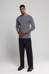 Langærmet stribet skjorte i marineblå og hvid bomuld med en rund halsudskæring. Kombineret med sorte bukser og sorte sko.