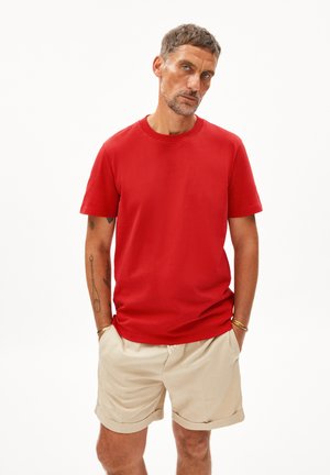 Rotes Baumwoll-T-Shirt mit kurzen Ärmeln, rundem Halsausschnitt und lockerem Schnitt, kombiniert mit beigen Shorts. Minimalistisches Design ohne sichtbare Muster.
