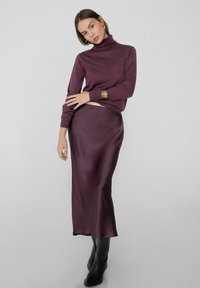Suéter burdeos de cuello alto en punto suave, combinado con una falda midi de satén burdeos y botines negros de tacón. Grandes pendientes de aro dorados.