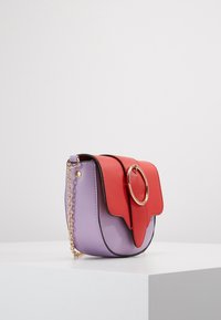 Fialová a červená syntetická kožená kabelka se zlatým kulatým kovovým detailem, má klopový vršek a řetízek na nošení. Hladký povrch.