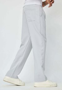 Pantalons en tissu gris clair à coupe droite, dotés de poches latérales et d'une poche arrière à rabat, associés à des baskets blanches.