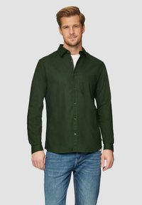 Donkergroene overhemd met lange mouwen, voorzien van een borstzak en een gladde textuur. Draag het over een wit T-shirt, gecombineerd met blauwe jeans.
