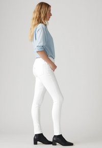 Camisa de mezclilla azul clara, con mangas enrolladas, combinada con unos jeans blancos de corte slim y botas negras de tobillo. Diseño simple con detalles de hardware mínimos.