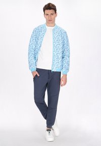 Giacca bomber azzurro chiaro con un motivo testurizzato, t-shirt bianca, pantaloni jogger blu navy e sneakers bianche. Presenta una chiusura a zip e polsini a coste.