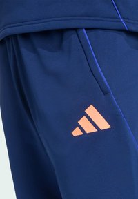 Marineblaue Sport Shorts mit blauen Akzenten und lebhaftem orangefarbenen Adidas-Logo. Hergestellt aus glattem, leichtem Material mit lockerem Schnitt.