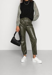 Pantaloni neri in ecopelle con vita alta, vest in maglia nera e camicia a maniche lunghe con fantasia. Borsa nera e sneaker piattaforma bianche.