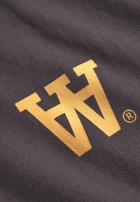 Dunkelgrauer Stoff mit einem markanten goldenen "W"-Logo und Markenzeichen. Die Textur ist glatt und gestrickt und weist ein klares Design auf.