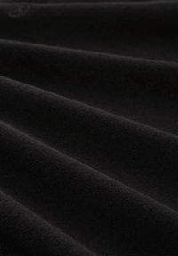 Tessuto nero con superficie morbida e testurizzata caratterizzata da sottili creste e onde. Il materiale appare leggero e liscio, evidenziando la profondità nelle pieghe.