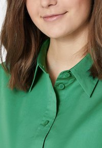 Grünes Button-Down-Hemd mit Kragen, aus glattem Stoff, mit passenden Knöpfen und einem schlichten Design.
