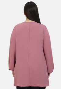 Top a maniche lunghe in morbido tessuto rosa chiaro con una superficie testurizzata, caratterizzato da un dettaglio nella cucitura posteriore e una vestibilità rilassata.