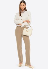 Giacca crema testurizzata con bottoni dorati, abbinata a pantaloni beige su misura. Accessoriata con una borsa a tracolla bianca e scarpe con tacco a blocco dorate.