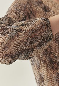 Bedruckte Bluse mit einem Schlangenledermuster in Braun-, Beige- und Schwarztönen; leichter, fließender Stoff mit gerafften Ärmelsäumen.