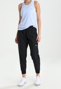 Lichtblauwe mouwloze sporttop met een ronde halslijn; zwarte tapered broek met elastische boorden; witte sportschoenen met gestructureerde zolen.