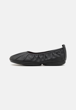 Ballerines en cuir noir avec des détails froncés sur les côtés, bout arrondi souple, semelle flexible et un logo subtil à l'arrière.