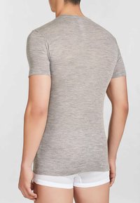 T-shirt grigia aderente a maniche corte realizzata in morbido tessuto a coste, con collo rotondo e una texture liscia. Indossata con pantaloni corti bianchi.