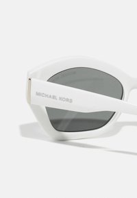 Valged Michael Kors-i prillid, millel on geomeetriline disain, tumedad läätsed ja kuldne detailimööda templite peal. Matte viimistlus.