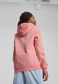 Felpa rosa con cappuccio, realizzata in tessuto morbido. Presenta una vestibilità comoda e polsini a costine, abbinata a pantaloni di denim azzurro.