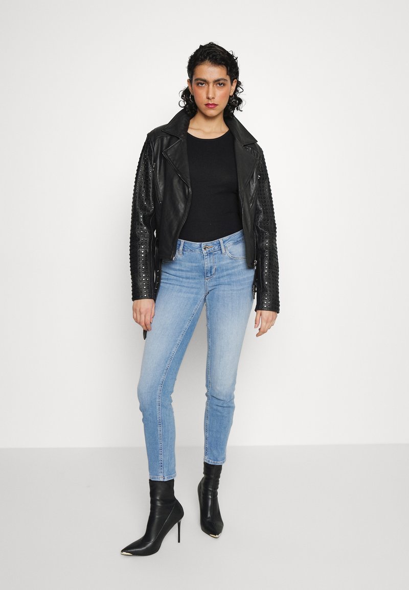 Schwarze Leder-Bikerjacke mit genieteten Ärmeln, kombiniert mit einem eng anliegenden schwarzen Oberteil und hellblauen Skinny-Jeans. Schwarze spitze Ankle-Boots sind ebenfalls enthalten.