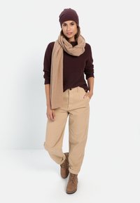 Brauner Pullover, beiger Schal, beige Baggy-Hosen und braune Schnürstiefel. Eine Wollmütze ergänzt das Outfit. Einfaches, lässiges Design.