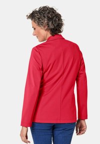 Rode jas met lange mouwen en een getailleerde pasvorm, voorzien van een notch kraag en een soepele textuur. Het achteraanzicht toont schone naden en een gestructureerd ontwerp.