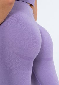 Hoch taillierte Leggings in einem hellen Lilaton, hergestellt aus dehnbarem, glattem Stoff, mit dezenten Texturen und konturierenden Designdetails.