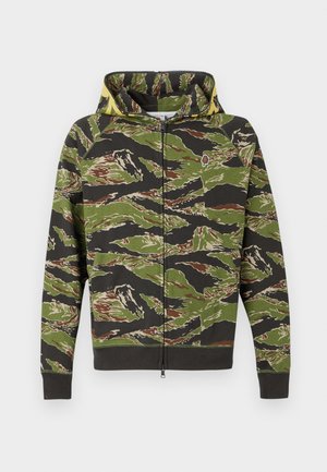 Sweat à capuche zippé avec un motif camouflage vert agrémenté de touches de marron et de noir. Doté de poignets et d'une taille côtelés, d'une texture lisse et d'un design pratique.