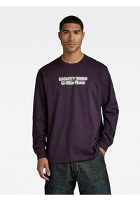 Langermet lilla skjorte med hvit tekst "EIGHTY NINE G-StarRaw" på fronten. Laget av mykt materiale med en avslappet passform.