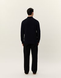 Marineblaues, geripptes Strickpolo mit Kragen, getragen zu schwarzen Hosen. Von hinten betrachtet, wodurch die volle Länge und Passform des Pullovers sichtbar wird.