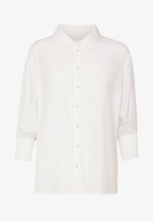 Bijela bluza s gumbima, klasičnim ovratnikom, tričetvrt rukavima i nabranim manšetama.