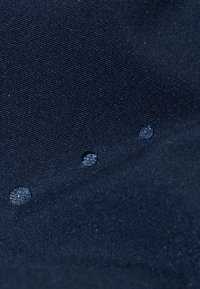 Tissu bleu marine foncé avec une surface texturée, présentant trois petites gouttes d'eau claires reposant dessus.