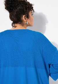 Blå stickad tröja med ett nätmönster på den övre delen och en enfärgad underdel. Tyget är texturerat och lätt.