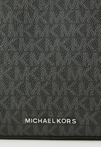 Čierna textúrovaná tkanina s jemným vzorom, na spodnej časti s nádychom striebra je umiestnené logo "MICHAEL KORS".
