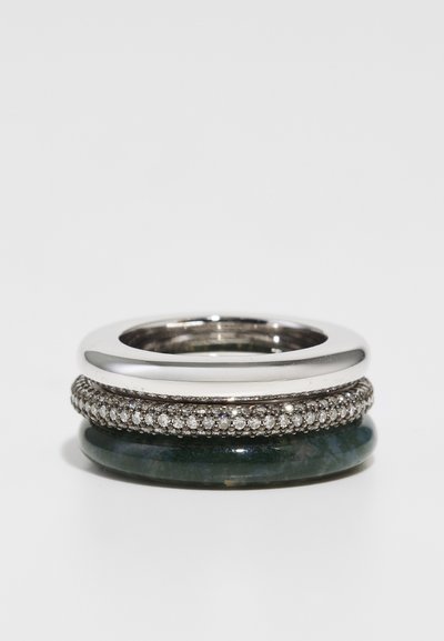 Anello impilato con una banda in argento lucido, una banda con pietra verde e una banda ornata di diamanti con dettagli intricati.