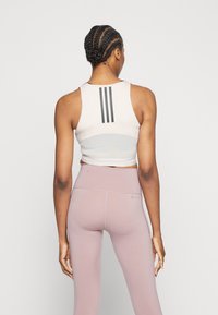 Světlý béžový sportovní podprsenka s třemi černými pruhy na zádech, spárovaná s bledě růžovými legínami s vysokým pasem; hladká textura, přiléhavý design.