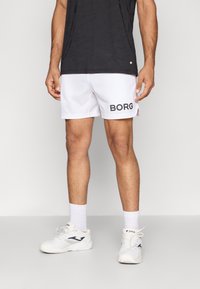 Bermudas brancas de desporto com o logo preto "BORG", tecido leve, cintura elástica. Usadas com ténis brancos e meias de cano curto.