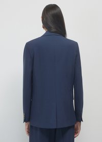 Veste bleu marine avec une fente unique, coupe ajustée et poignets boutonnés. Tissu lisse avec une silhouette élégante et un design minimaliste.