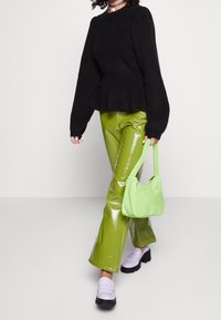 Schwarzer Strickpullover, grüne glänzende Hose, helllila Mokassins und eine weiche grüne Handtasche. Langer Ärmel und Peplum-Design am Pullover.