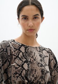 Top cu mânecă lungă dintr-un material moale, de catifea, având un model de imprimeu în culorile negru și bej, cu umeri adunați și un guler rotund.