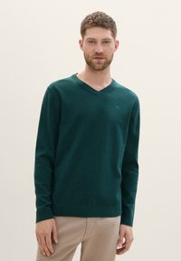 Pulover v-neck de culoare verde închis, realizat dintr-un material moale, cu mâneci lungi și tiv ribflat. Design minimalist cu detalii discrete ale logo-ului.