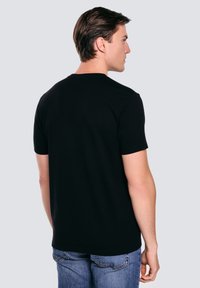 Černé bavlněné tričko s krátkým rukávem, kulatým výstřihem a hladkým povrchem. Model stojí zády, na sobě má modré džíny.