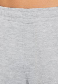 Un pantalon de survêtement gris clair en tissu doux, présentant une texture lisse, une taille élastique et une poche latérale avec un détail de couture subtil.